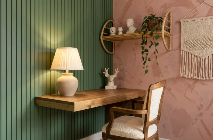 Coin bureau décoré tendance avec mur en plâtre strié vert sauge, étagère en rotin et plantes suspendues pour une ambiance intérieure contemporaine